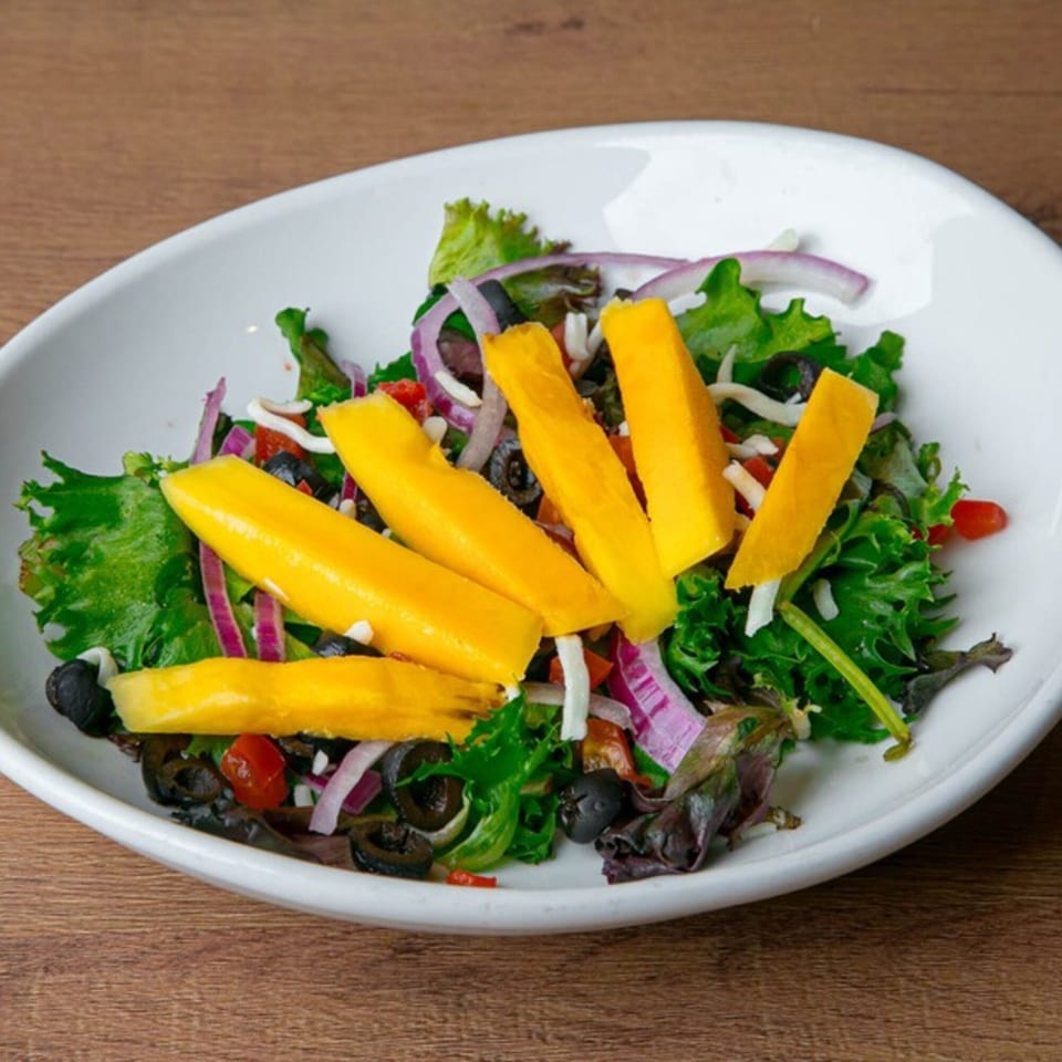 Fresh Desi Aroma salad with mango slices, red onions, black olives, and mixed greens.