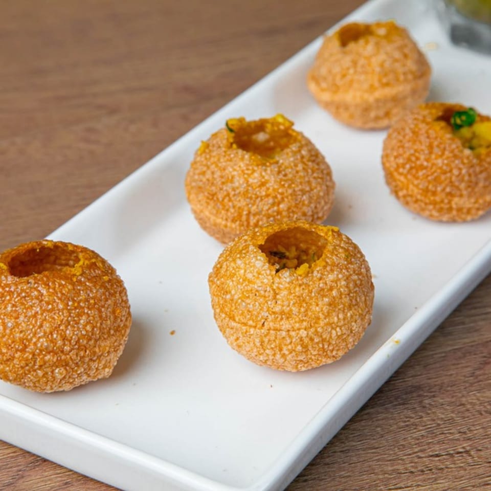 Five golden-brown pani puri shells, some filled, arranged on a white rectangular plate.