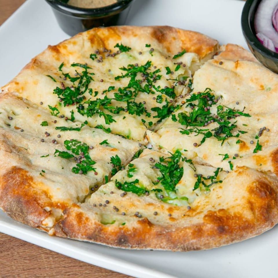 Indian naan bread, topped with fresh green herbs and mustard seeds, served on a white plate.