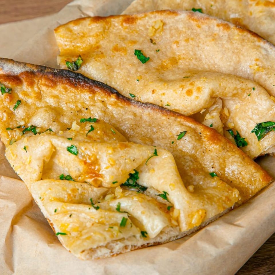 Golden brown garlic naan bread, garnished with fresh green herbs, served on parchment paper.