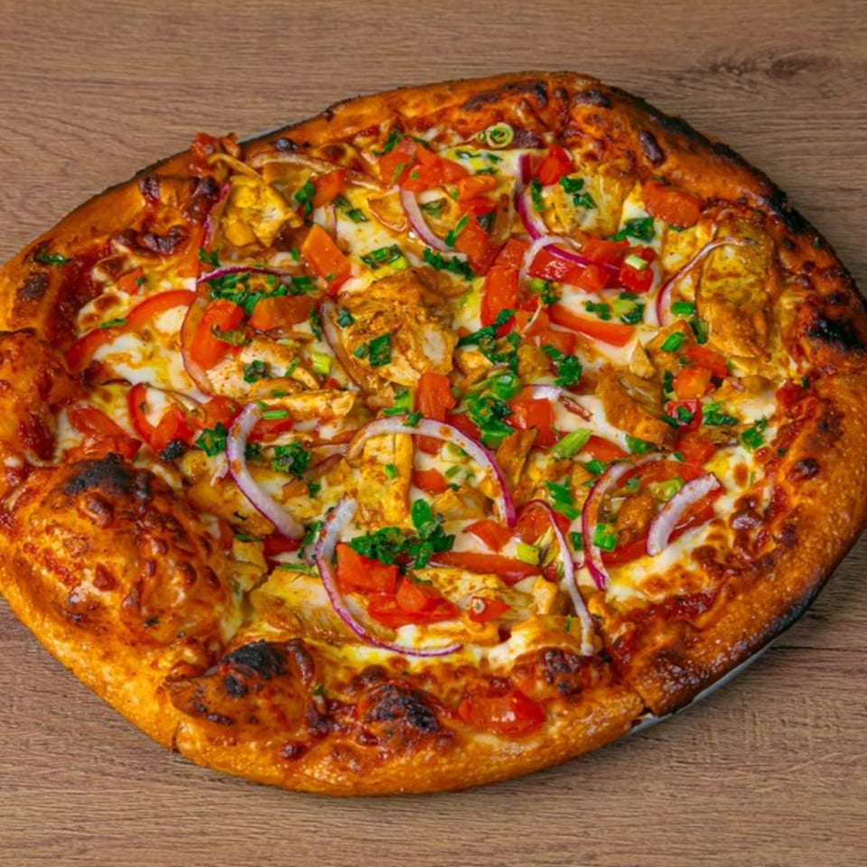 A Desi Aroma Indian pizza, topped with chicken, red onions, tomatoes, and green herbs.